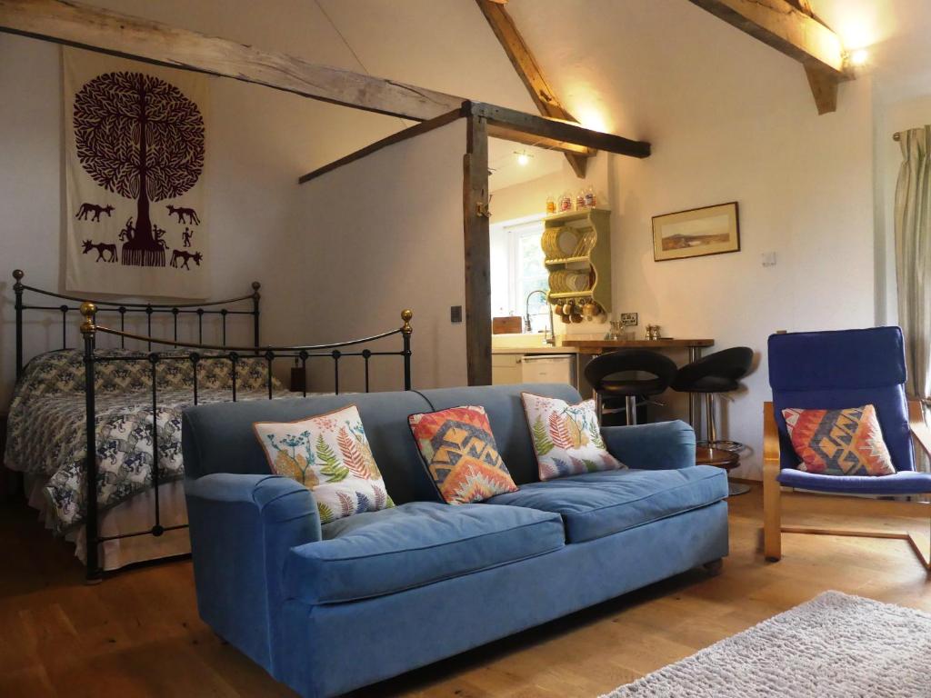 a living room with a blue couch and a bed at Rural 17th century barn studio apartment in Cheriton Bishop