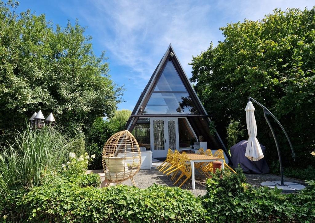 een klein glazen huisje met een tafel en stoelen in een tuin bij Vakantiehuis in paradijselijke sfeer met privémeertje in Kleve