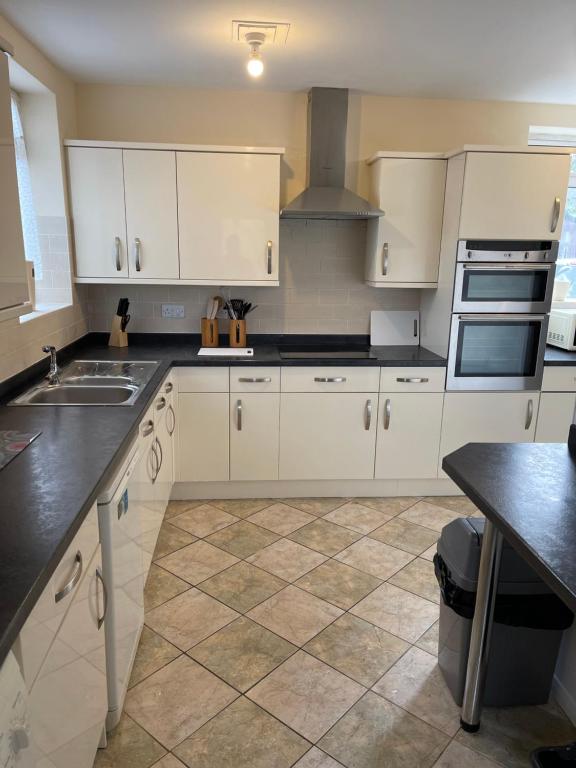 Spacious 9 bed house in Mansfield Nottinghamshire في مانسفيلد: مطبخ بدولاب بيضاء وأرضية بلاط