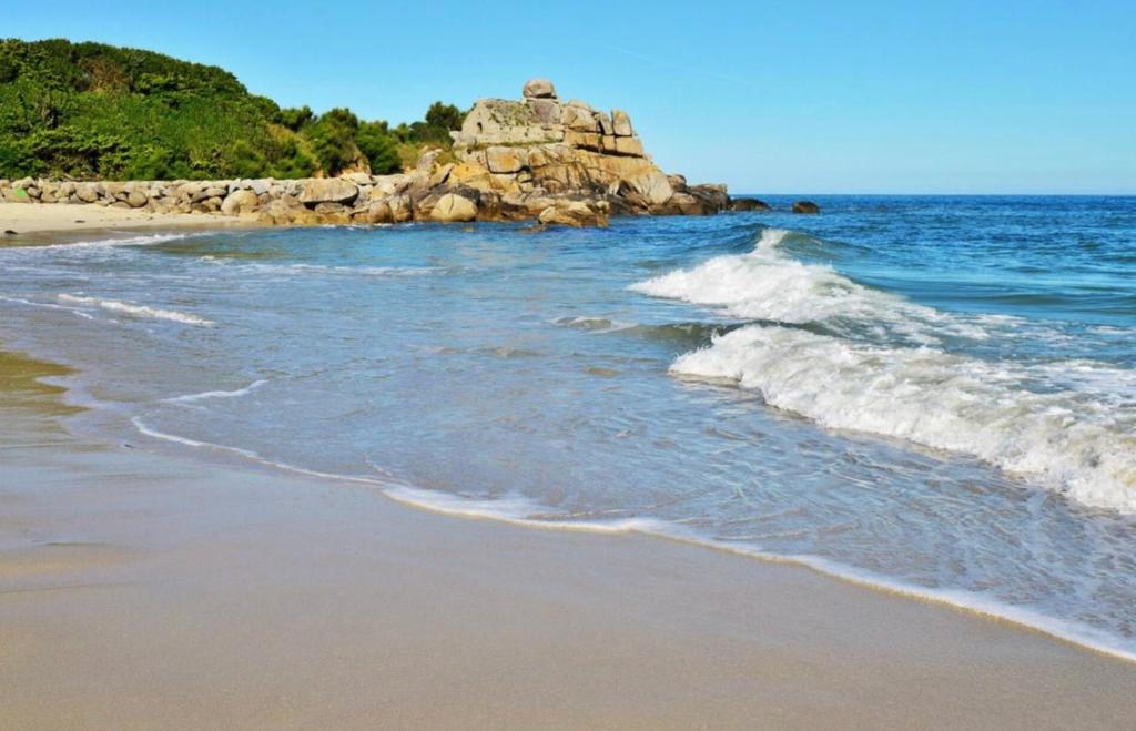 a beach with waves and a rock in the ocean at Le Penty de Kerfissien, Studio de plage 2 étoiles in Cléder