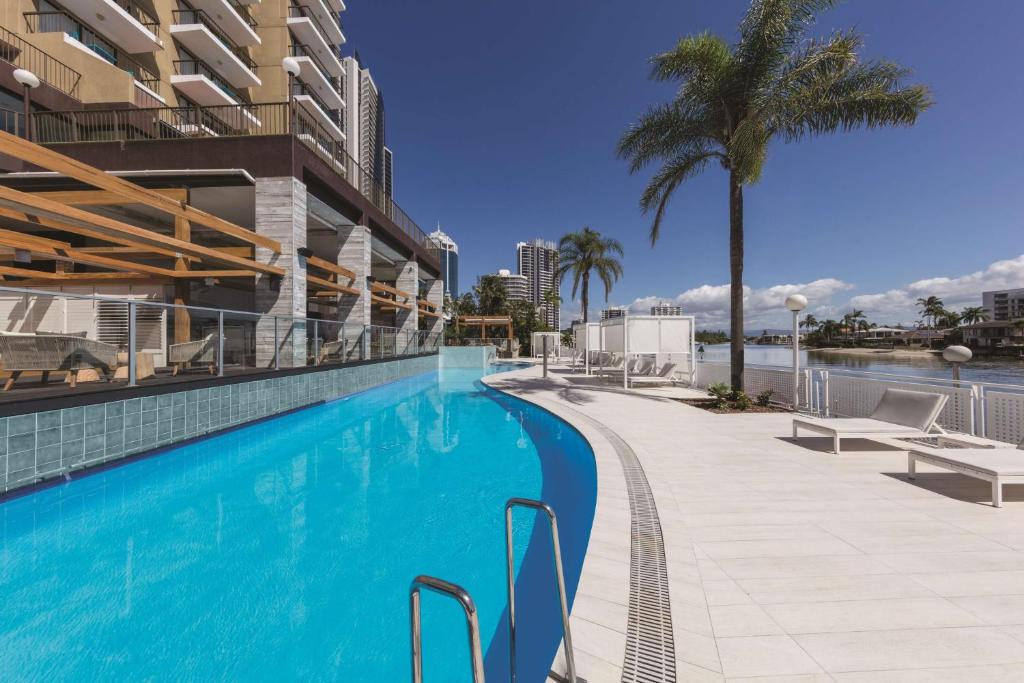 a swimming pool next to a building with a palm tree at Vibe Hotel Gold Coast in Gold Coast