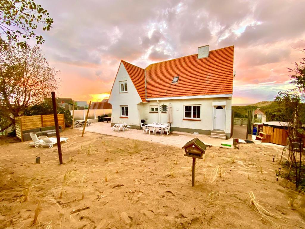 une maison blanche avec un toit rouge dans une cour dans l'établissement Villa Friedolin heeft zicht op zee en duinen, in duinenreservaat, hot tub met jacuzzi en sauna met zeezichten te Oostduinkerke, à Oostduinkerke