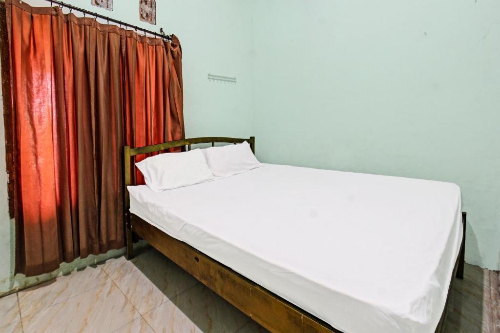 a bed in a room with a red curtain at SPOT ON 91771 Homestay Bang Haji in Praya