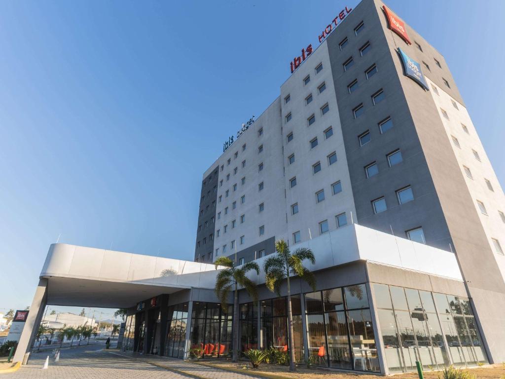 a hotel building with palm trees in front of it at Ibis Lorena - Circuito da Fé in Lorena