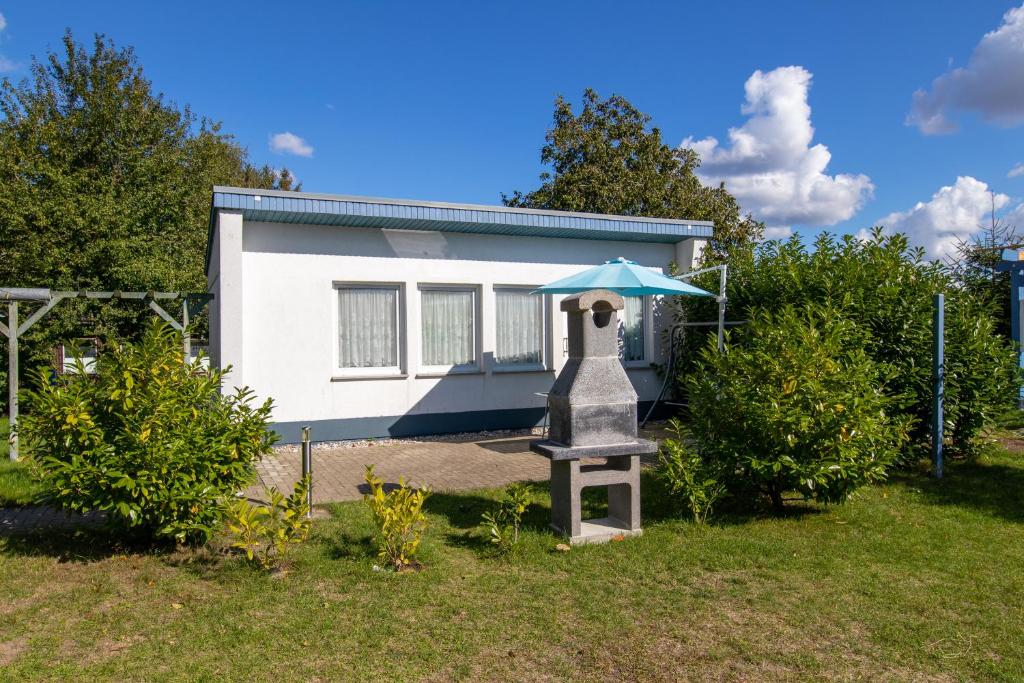 a small house with a blue umbrella on top of a yard at Bungalow am Waldrand in Barth