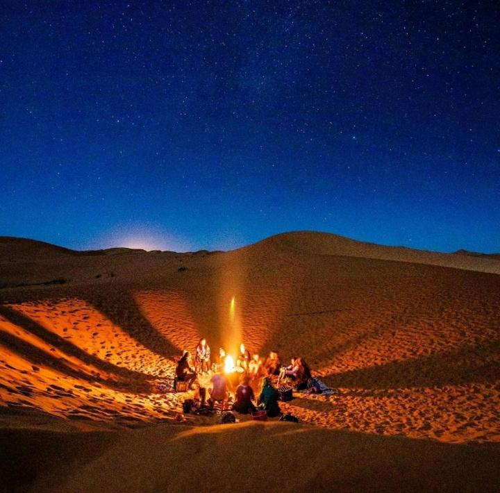 un grupo de personas sentadas alrededor de un fuego en el desierto en Mhamid camp activités en Mhamid