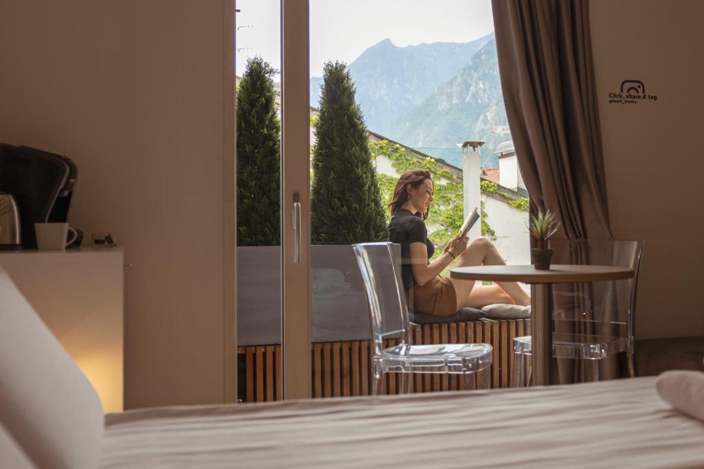 Una donna seduta a un tavolo in una stanza d'albergo che guarda fuori dalla finestra di HEART OF TRENTO Loft & Rooms a Trento