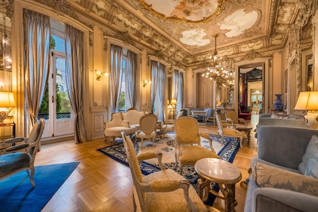 An ornate salon lined with seating, mirrors and tall French doors.