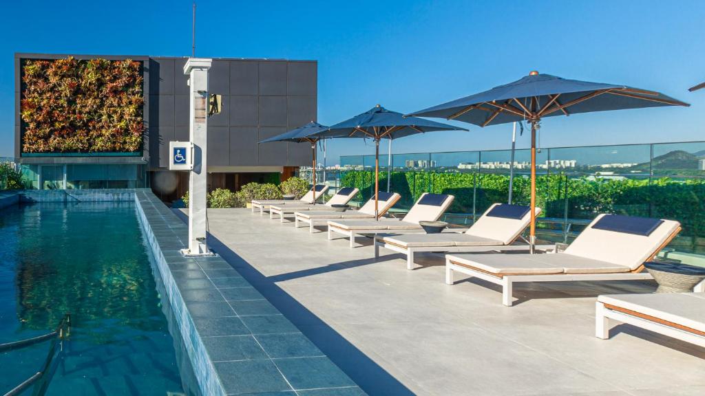 eine Reihe von Liegestühlen und Sonnenschirmen neben einem Pool in der Unterkunft Venit Barra Hotel in Rio de Janeiro