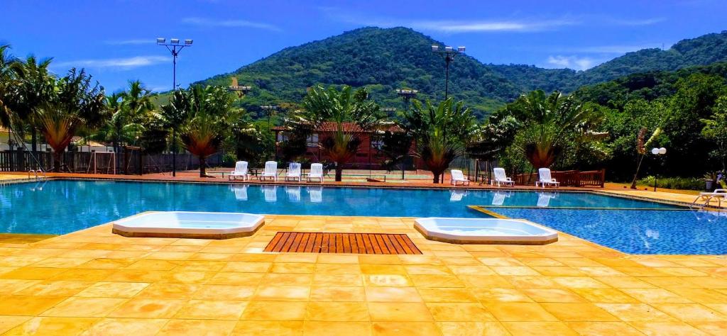 a swimming pool with chairs and a mountain in the background at Maresias Beach House - Casas de alugueis em cond beira mar in Maresias