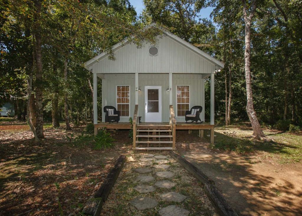 una piccola casa bianca con due sedie nel bosco di Porch Lane Cottage F a Fairhope
