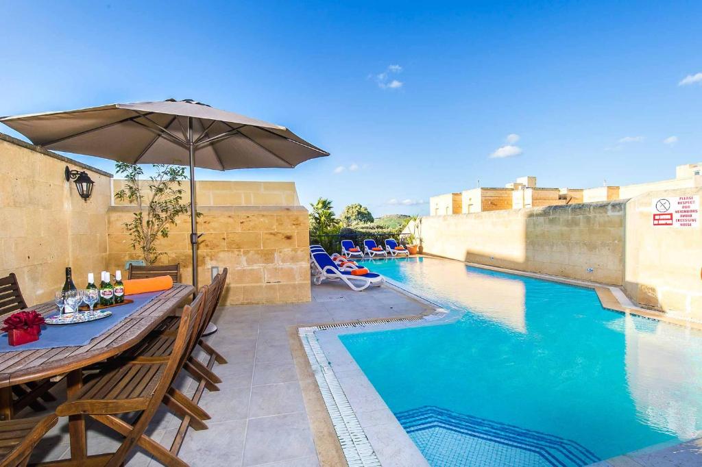 a table with an umbrella next to a swimming pool at Four Winds Holiday Home in Kerċem
