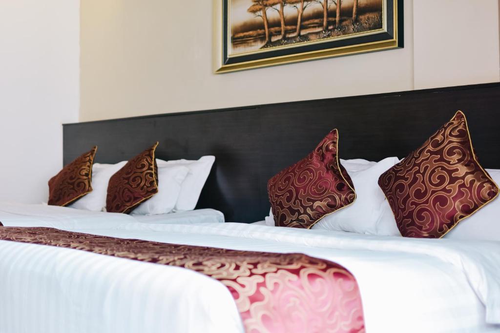 2 letti in camera d'albergo con cuscini rossi e marroni di J Suites Hotel a Kuala Terengganu