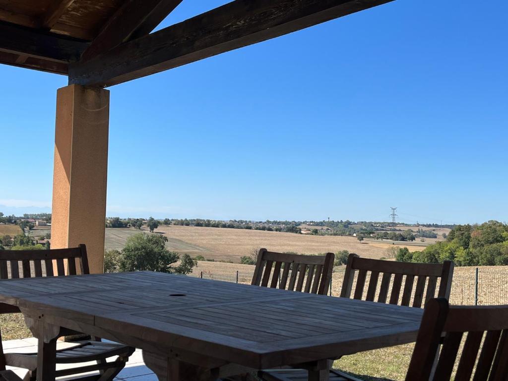 a wooden table on a porch with a view of a field at Jolie villa au cœur du Lauragais in Lanta