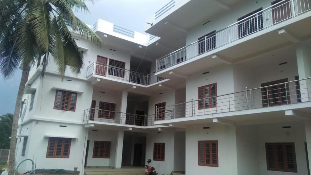 a large white building with balconies and a palm tree at Wayanad Biriyomz Residency, Kalpatta, Low Cost Rooms and Deluxe Apartment in Kalpetta