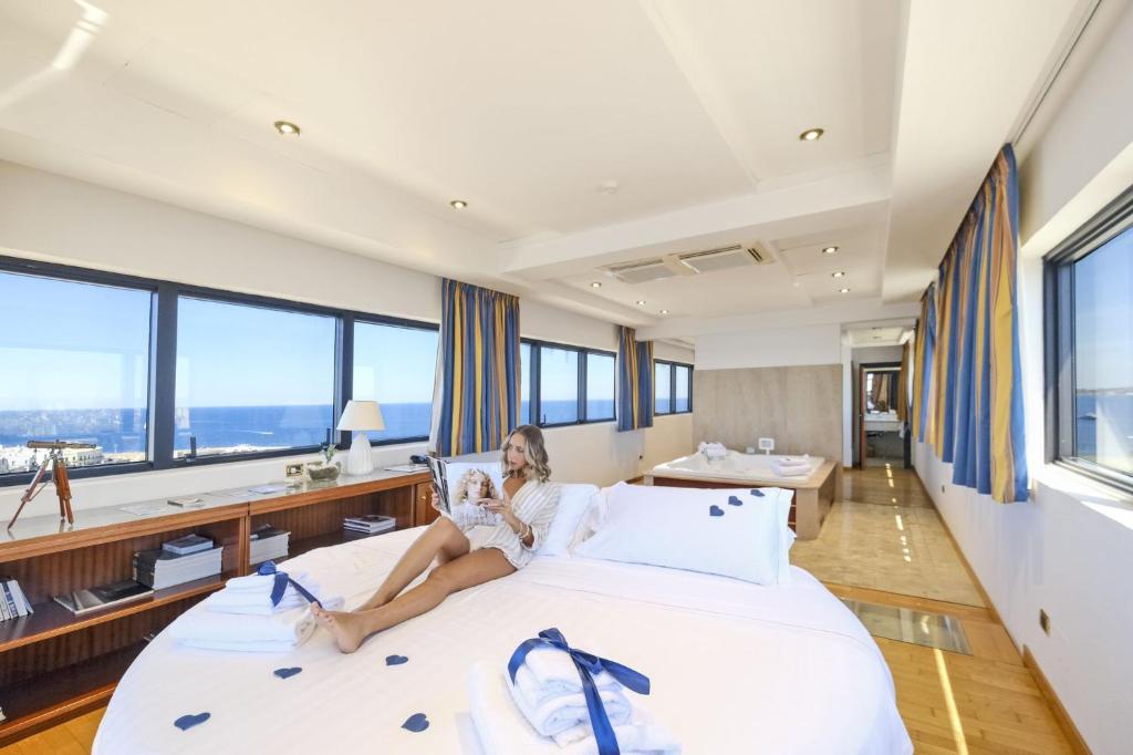 una mujer sentada en una cama en una habitación con ventanas en Hotel Bellavista Club-Caroli Hotels, en Gallipoli