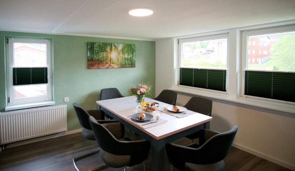 ein Esszimmer mit einem Tisch, Stühlen und Fenstern in der Unterkunft Ferienwohnung Ravensberg Dachgeschoss in Bad Sachsa