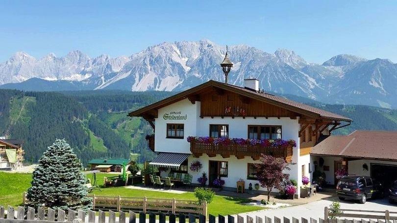 a building with flowers on the balcony with mountains in the background at Haus Steirerland in Schladming