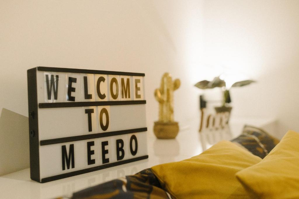 a sign that says welcome to meebo next to a bed at meebo apartments in Novi Sad