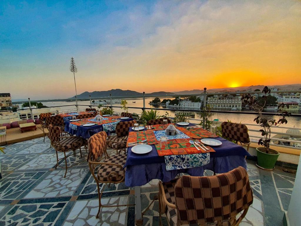 a deck with tables and chairs on a balcony with the sunset at Hotel Mewar Haveli - At Lake Pichola in Udaipur