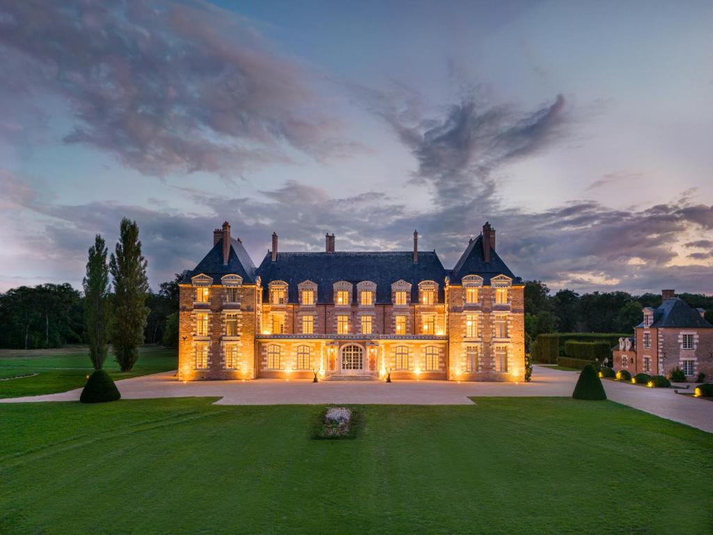 Una gran mansión con sus luces encendidas al anochecer en La Borde en Sologne Château & Spa en Vernou-en-Sologne