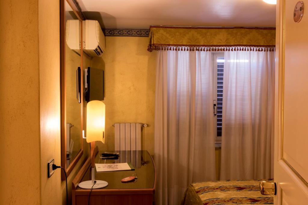 a room with a bed, desk, mirror and a lamp at Hotel Joli in Palermo