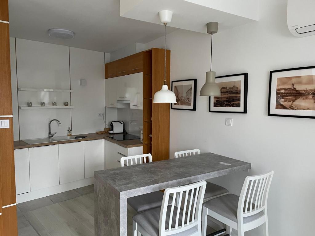 een keuken met een tafel, witte kasten en witte stoelen bij Quelle-Apartman in Győr