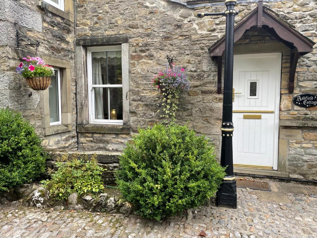 a stone house with a white door and flowers at Ashfield House in Grassington