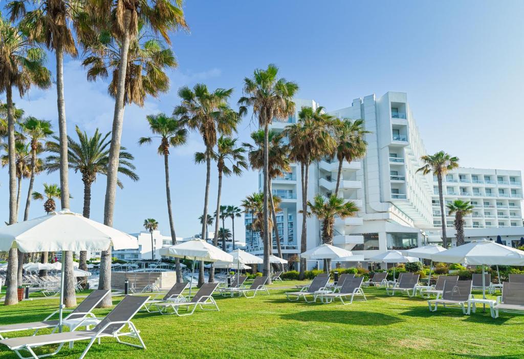 a lawn with chairs and palm trees and a building at Leonardo Plaza Cypria Maris Beach Hotel & Spa in Paphos City