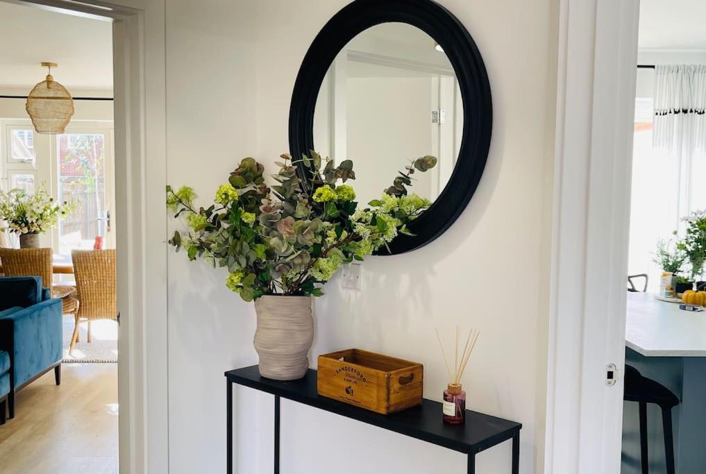 NEW! Beautiful contemporary property in Holt, Norfolk في هولت: مرآة و مزهرية مع الزهور على طاولة
