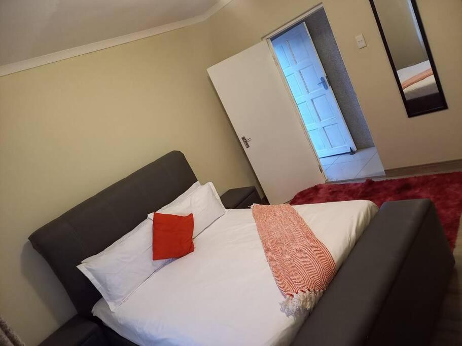 Comfy hidden home in Mthatha في امتاتا: غرفة نوم بسرير ذو شراشف بيضاء ومخدات حمراء
