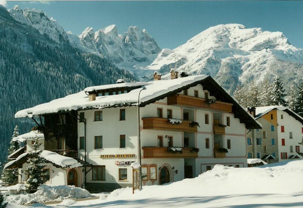 un edificio en la nieve con montañas en el fondo en Hotel Garnì Miramonti en Falcade