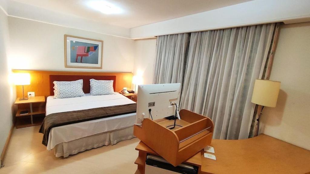 ein Hotelzimmer mit einem Bett und einem Schreibtisch mit einem Computer in der Unterkunft Flat Bienal Ibirapuera UH403 in São Paulo