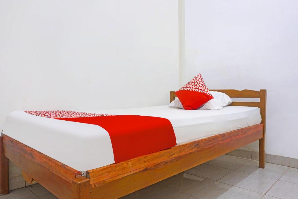 ein Holzbett mit roten und weißen Kissen darauf in der Unterkunft SPOT ON 91786 Kilana Homestay in Makassar