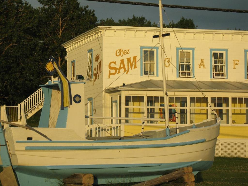 un barco está sentado frente a un edificio en Auberge du Café chez Sam en Baie-Sainte-Catherine