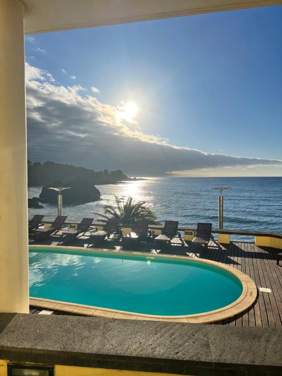 a swimming pool with chairs and the ocean in the background at Vinha da Areia Beach Hotel in Vila Franca do Campo