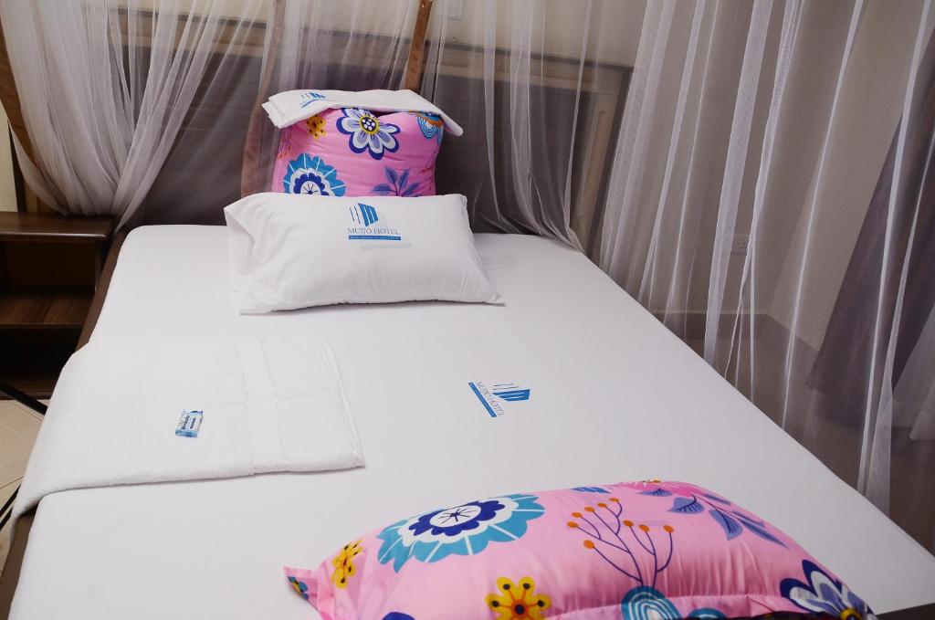 a bed with white sheets and floral pillows at Mujjo Hotel Kajjansi in Kampala
