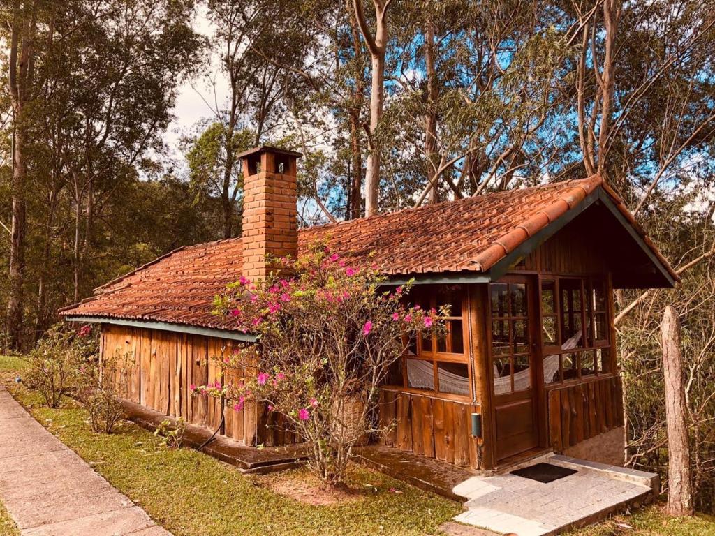 een klein houten huis met een stenen schoorsteen en bloemen bij Casa da Colina Chalés in Visconde De Maua