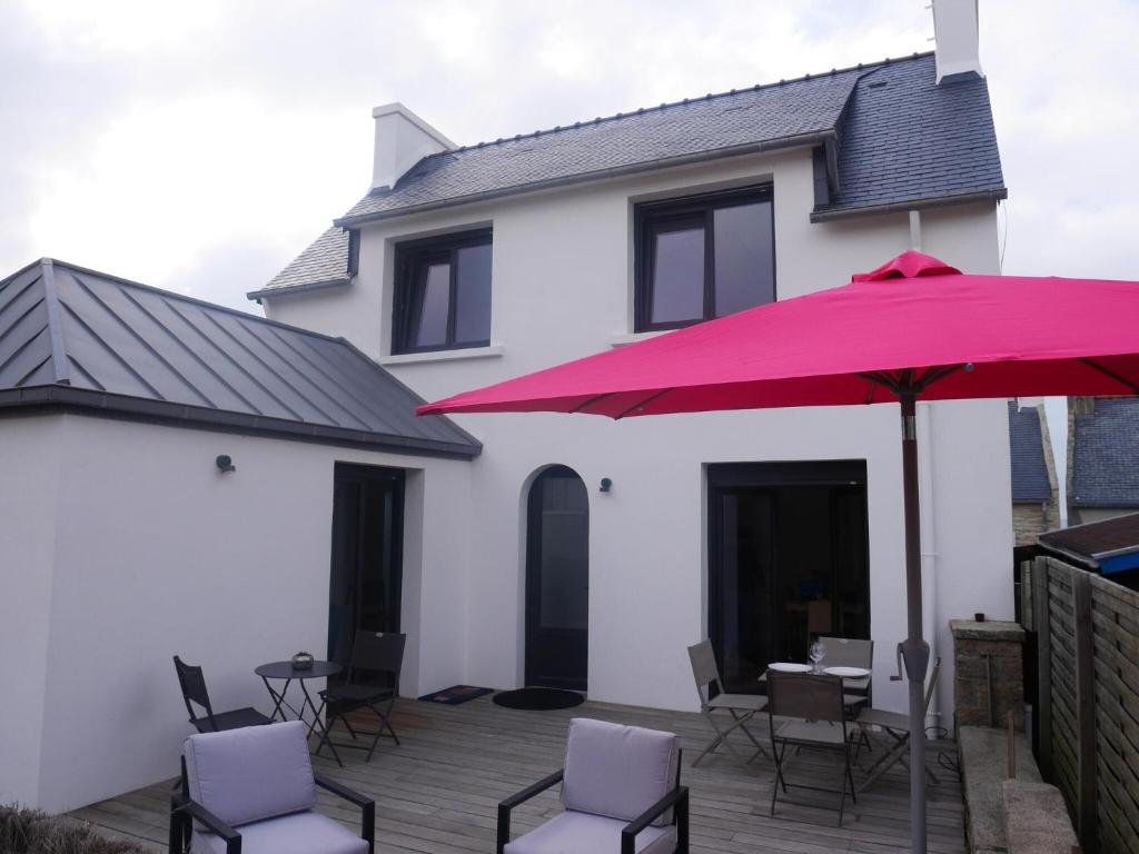 eine Terrasse mit einem roten Sonnenschirm und Stühlen sowie ein Haus in der Unterkunft Beachfront Holiday Home, Penmarch-St Guénolé in Penmarcʼh