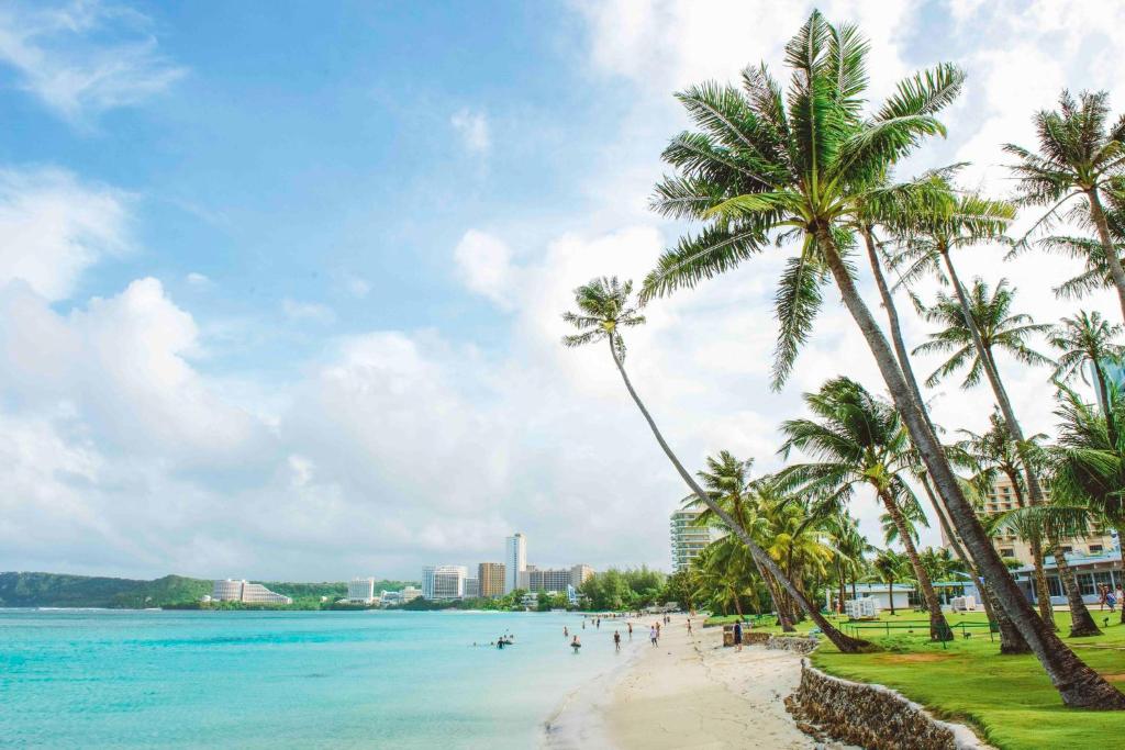 Crowne Plaza Resort Guam في تومون: شاطئ فيه نخيل وناس في الماء