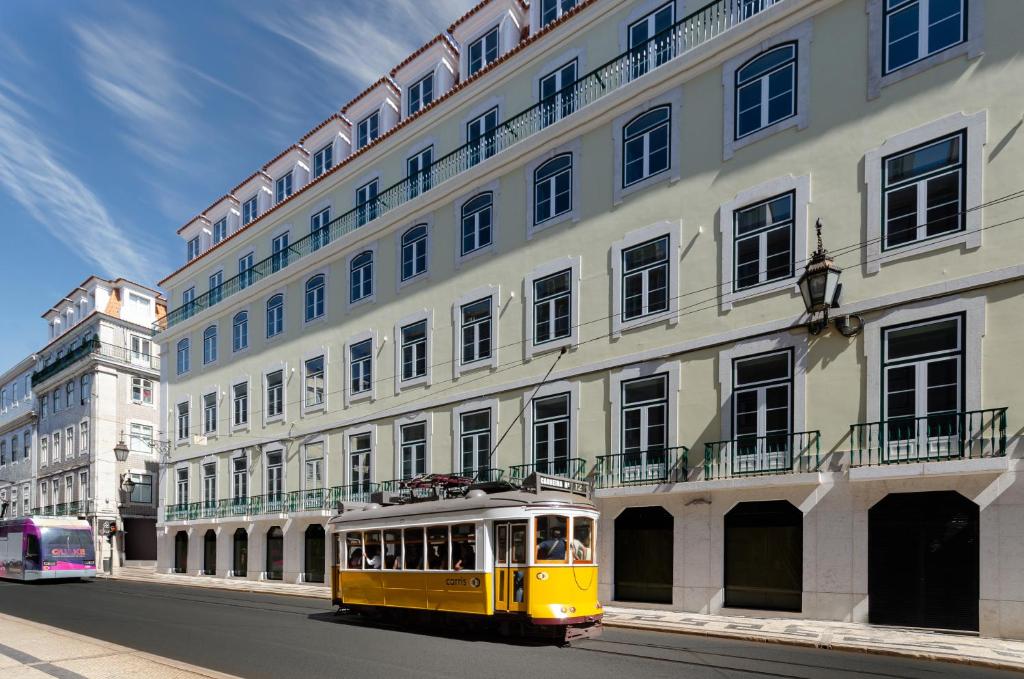 eine gelbe Straßenbahn, die an einem großen Gebäude vorbeifährt in der Unterkunft Eurostars Lisboa Baixa in Lissabon