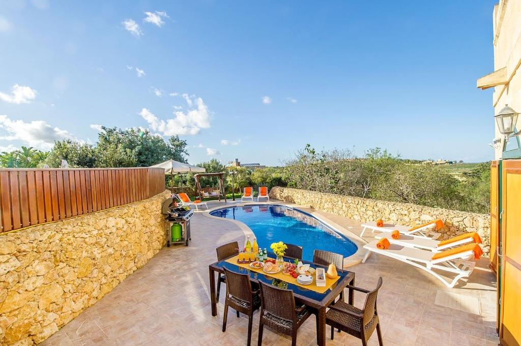 eine Terrasse mit einem Tisch und Stühlen neben einem Pool in der Unterkunft Rebbiegha Holiday Home in Qala