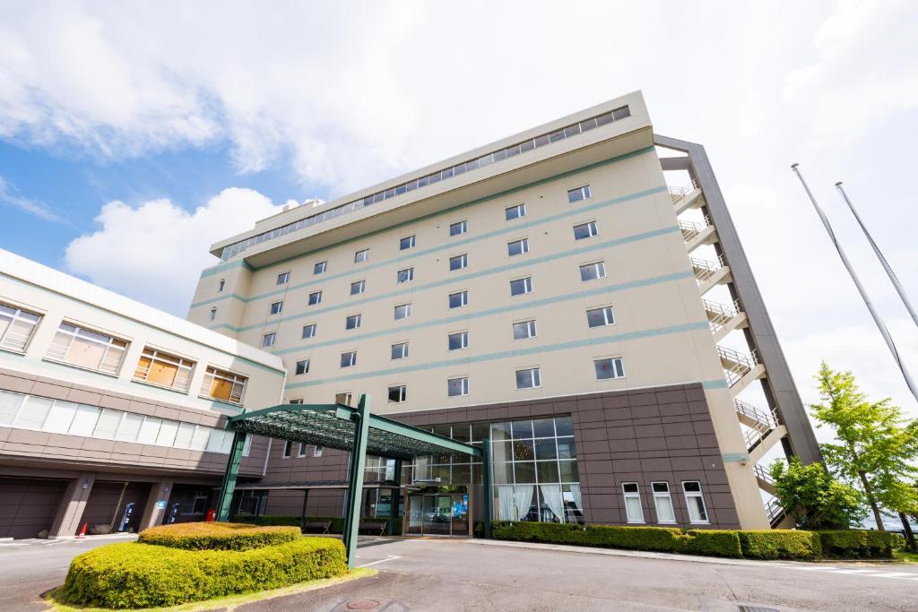 un gran edificio blanco con un refugio verde delante de él en KAMENOI HOTEL Yaizu, en Yaizu