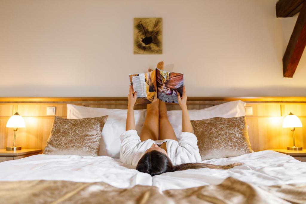 una mujer acostada en una cama leyendo un libro en Hotel Historia & Historante, en Veszprém