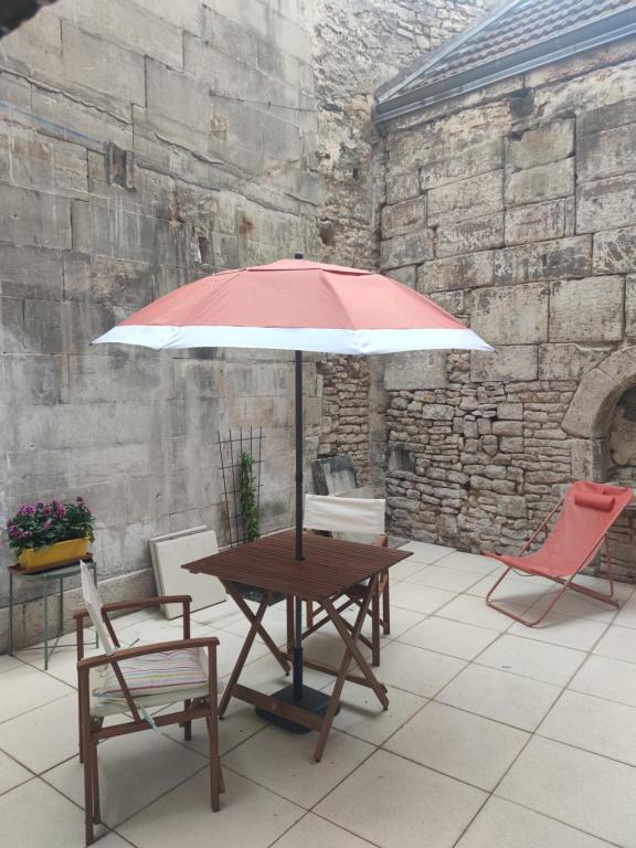 a wooden table with a red and white umbrella and chairs at Studio de charme, au calme dans le vieux Chaumont in Chaumont