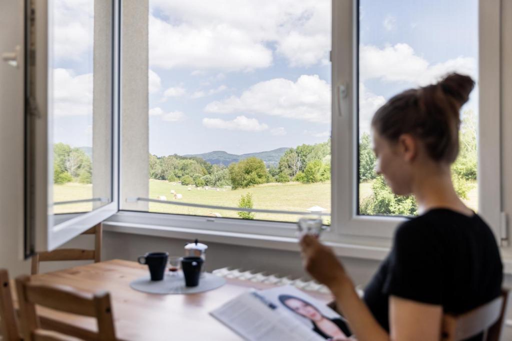 a woman sitting at a table in front of a window at Apartman JakoDoma vlastní parkování u domu ZDARMA in Česká Lípa