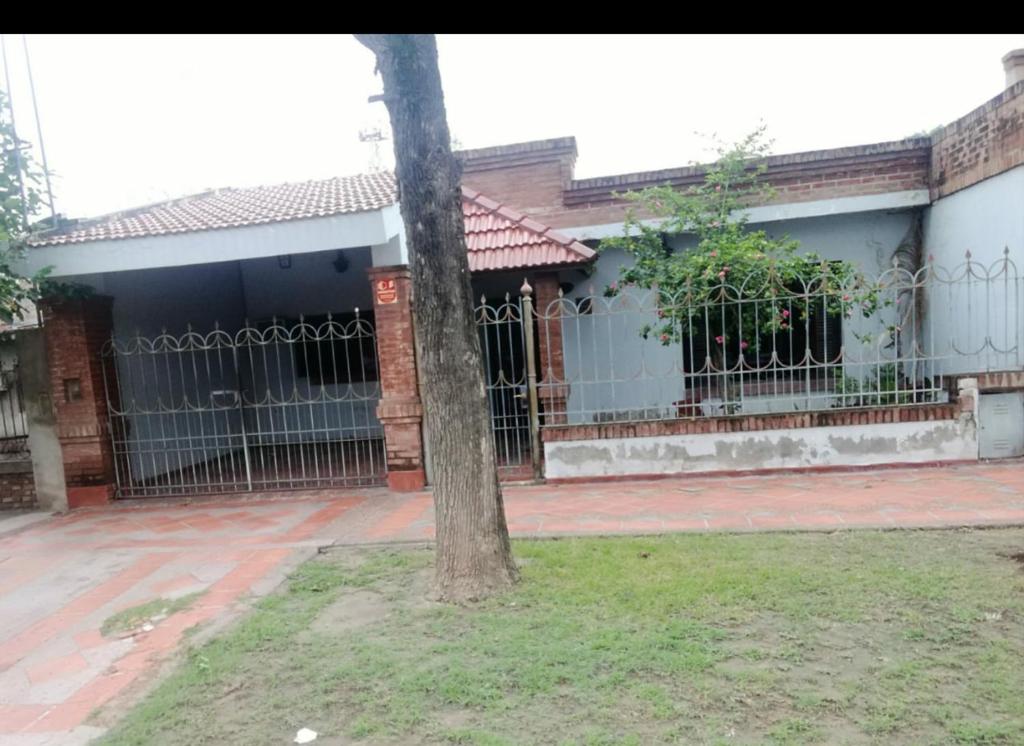 une maison avec une clôture et un arbre dans la cour dans l'établissement Avellaneda la banda, à La Banda