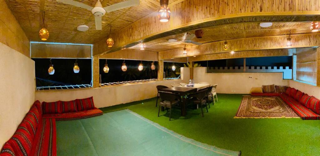 una stanza con tavolo, divani rossi e pavimento verde di Sehma Guest House a Al Ḩamrāʼ