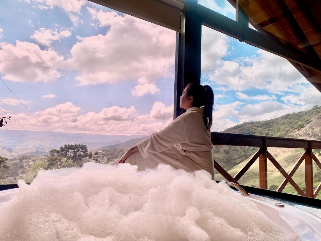 a woman sitting in a window looking out at the mountains at Chalé Luar da Mantiqueira in Sapucaí-Mirim