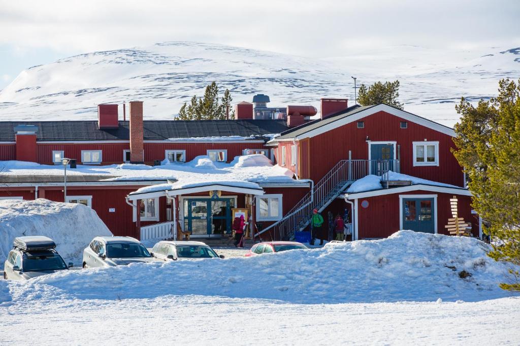 un edificio rojo con coches aparcados en la nieve en STF Grövelsjön Fjällstation & Hotell en Grövelsjön